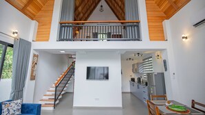 Uma sala de estar ampla com uma escada que leva a uma varanda, uma área de jantar e uma cozinha.