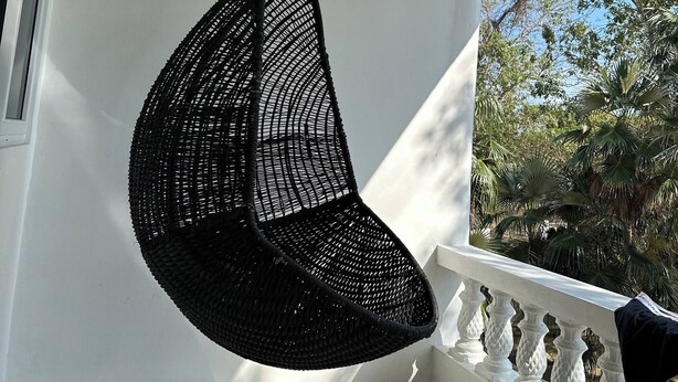 Una silla colgante en un balcón con barandilla blanca y vista a árboles.