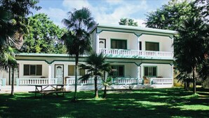 Un edificio de dos pisos con balcón, rodeado de palmeras y follaje.