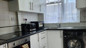 Una cocina moderna con armarios blancos, horno empotrado, lavadora y ventana con cortinas translúcidas.