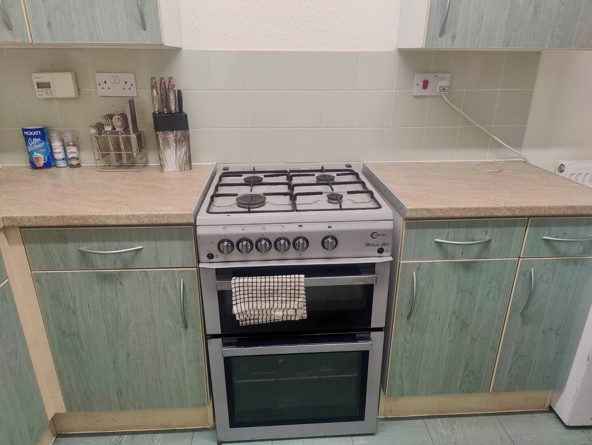 Una cocina con estufa a gas, microondas y horno empotrado. Hay armarios con manijas, una encimera y algunos utensilios de cocina.