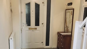 Un couloir avec une porte blanche, une commode en bois et un luminaire au plafond.