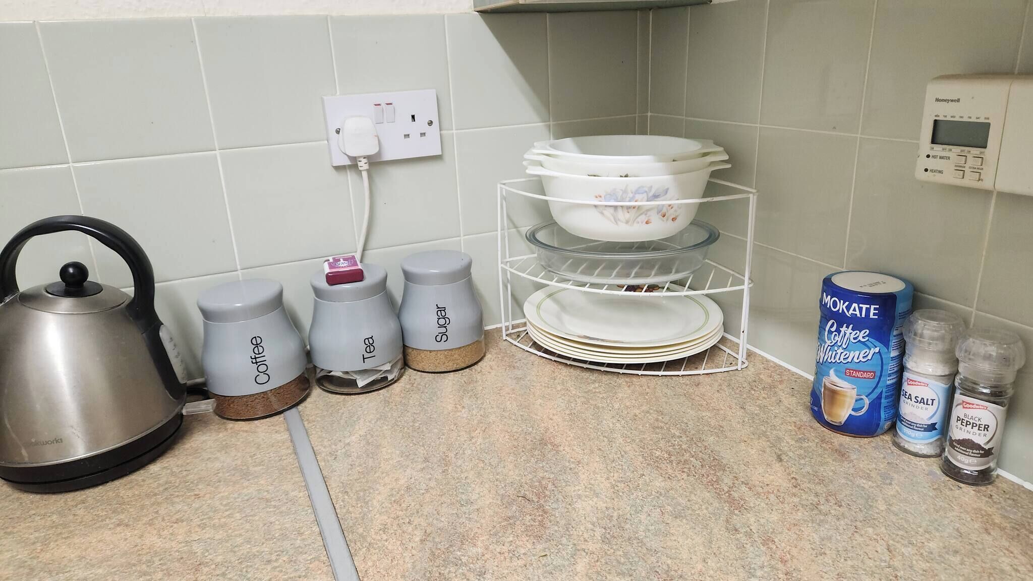 A kitchen with a kettle, sugar, coffee, and tea containers, a dish rack, and coffee-making supplies.