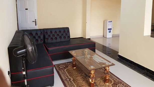 Una sala de estar con un sofá seccional negro, una mesa de centro de vidrio y un ventilador de pie.