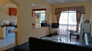 Una sala de estar con sofá, televisión, ventilador y una zona de cocina con estufa y fregadero.