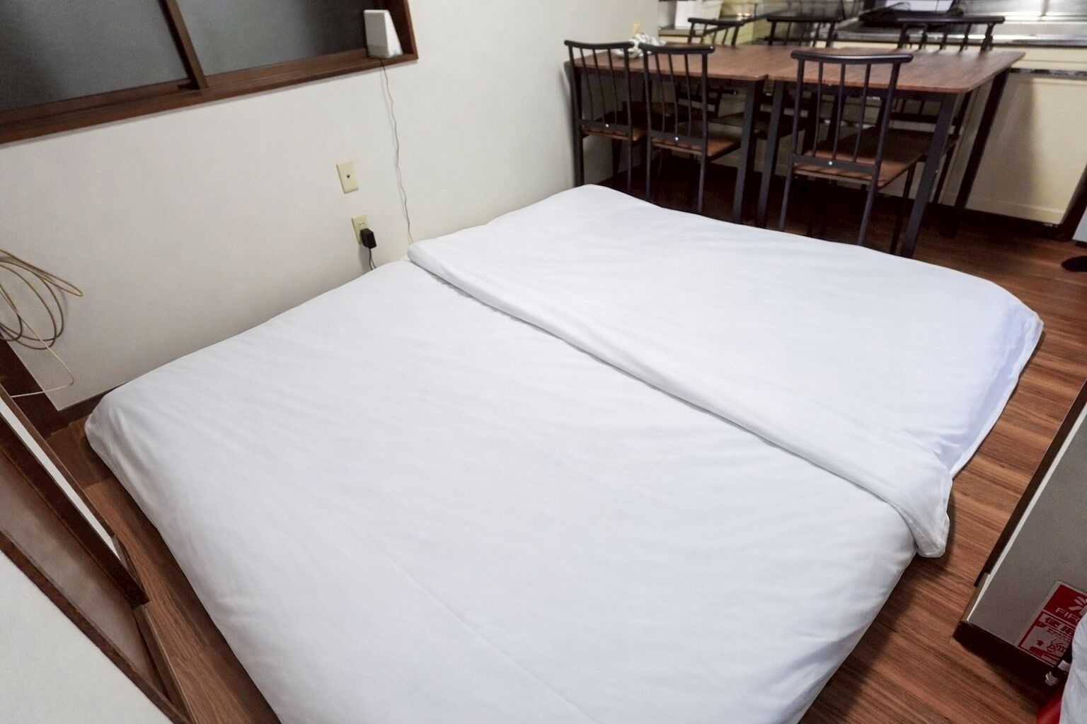 A single bed with white bedding in a room with a wooden floor, a desk, and chairs.