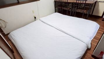 A single bed with white bedding in a room with a wooden floor, a desk, and chairs.