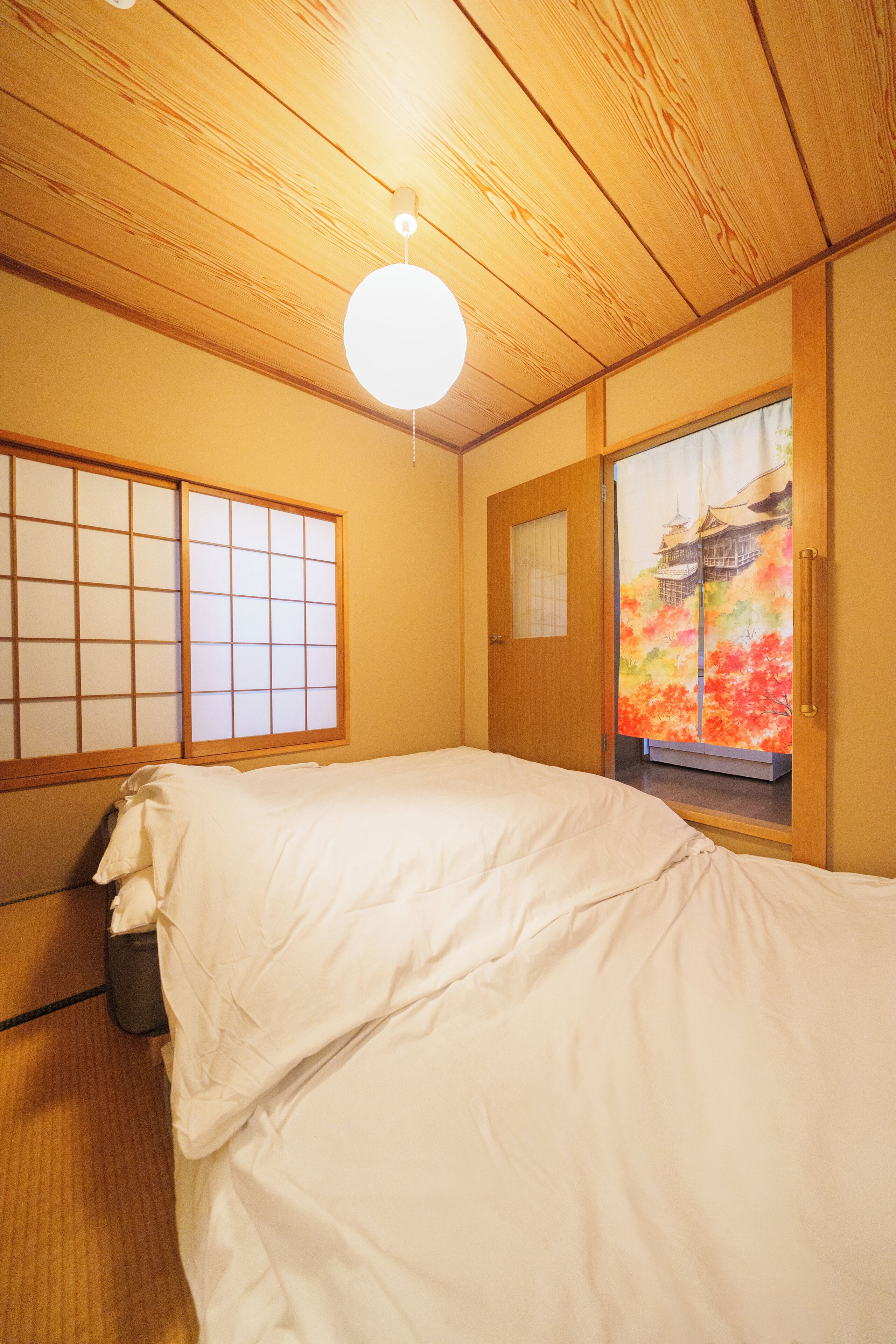 A traditional Japanese-style room with tatami flooring, a futon bed, shoji screens, and a sliding door with a view of a colorful landscape.
