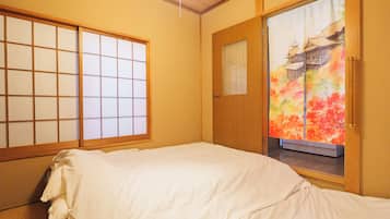 A traditional Japanese-style room with tatami flooring, a futon bed, shoji screens, and a sliding door with a view of a colorful landscape.