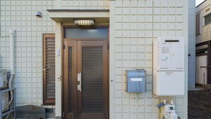 Entrada de un edificio con puerta marrón, pared con azulejos y cajas eléctricas.