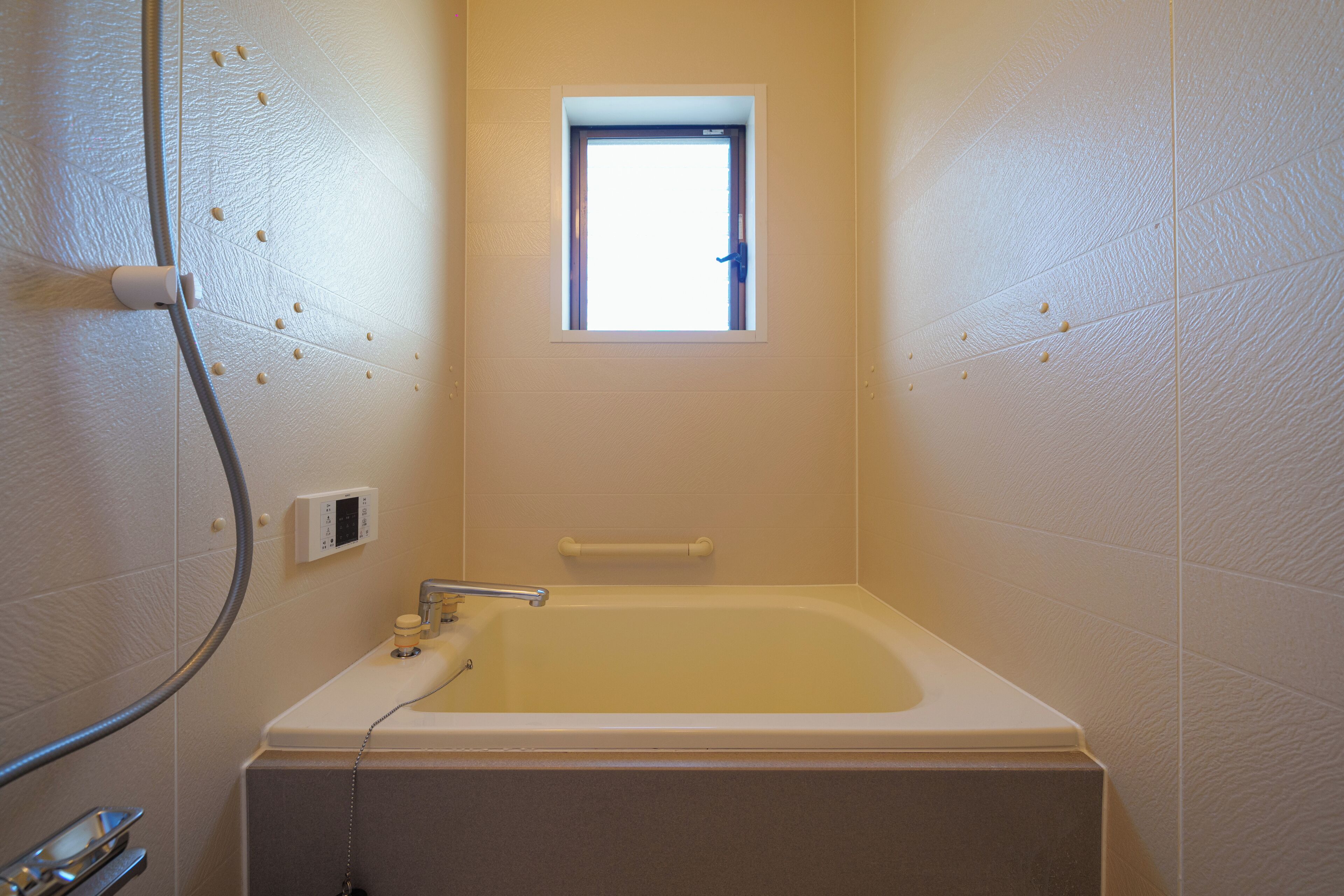 A small bathroom with a bathtub, a window, and a shower hose.