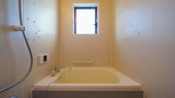 A small bathroom with a bathtub, a window, and a shower hose.