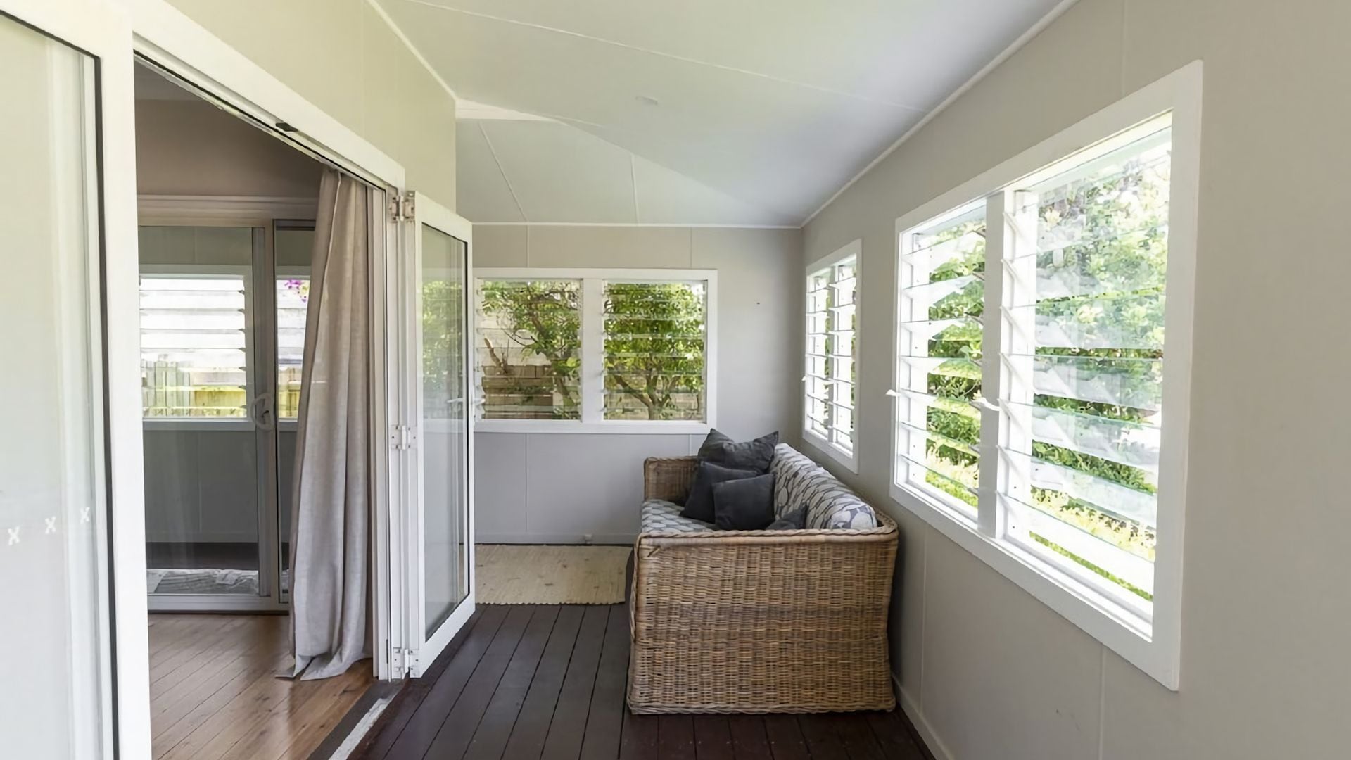 A balcony with a wicker sofa, a sliding glass door, and a view of greenery.
