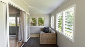 Ein Balkon mit einer Rattan-Couch, einer Schiebetür aus Glas und Blick ins Grüne.