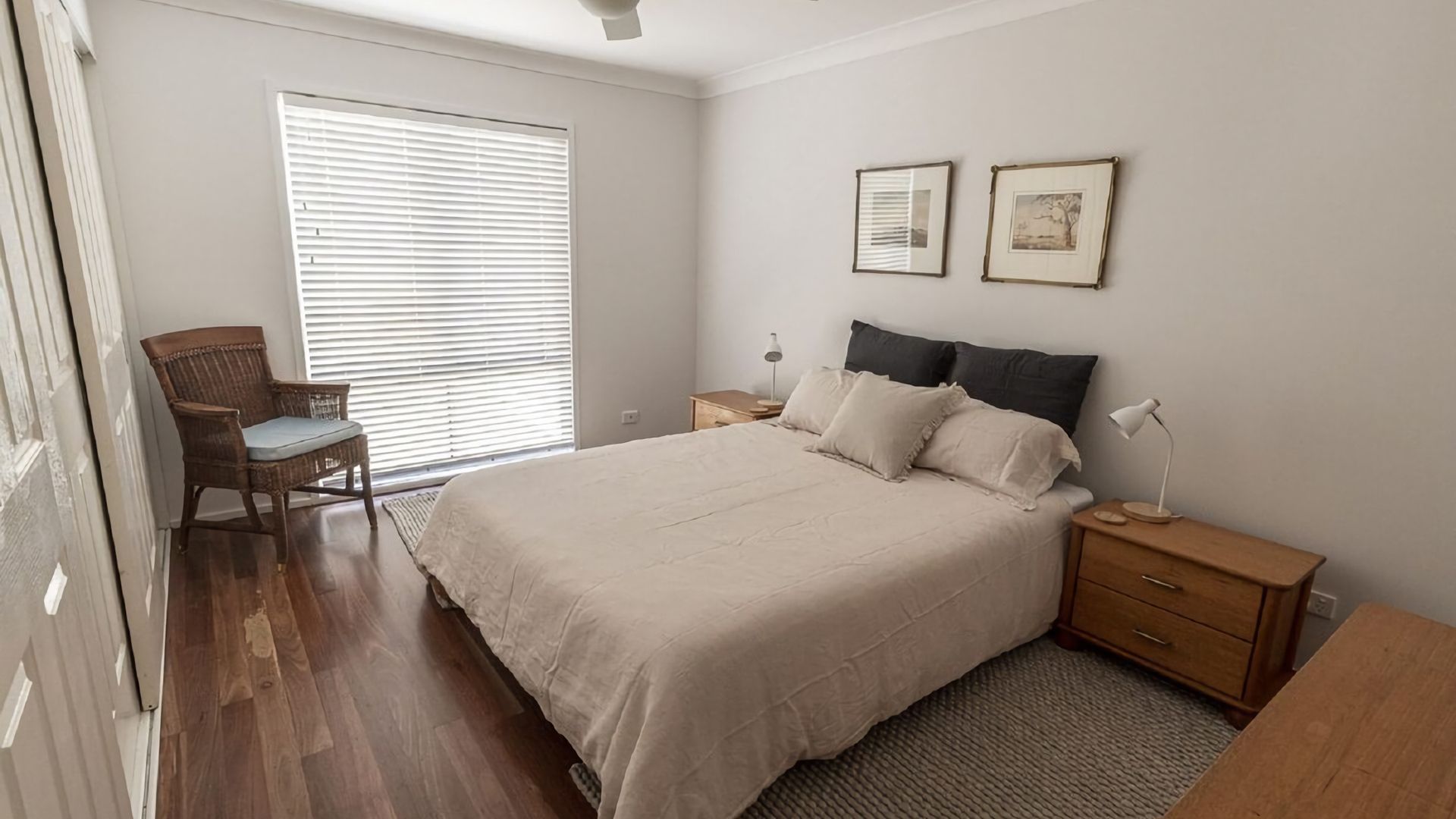 A bedroom with a large bed, a chair, a bedside table with a lamp, and two framed pictures on the wall.
