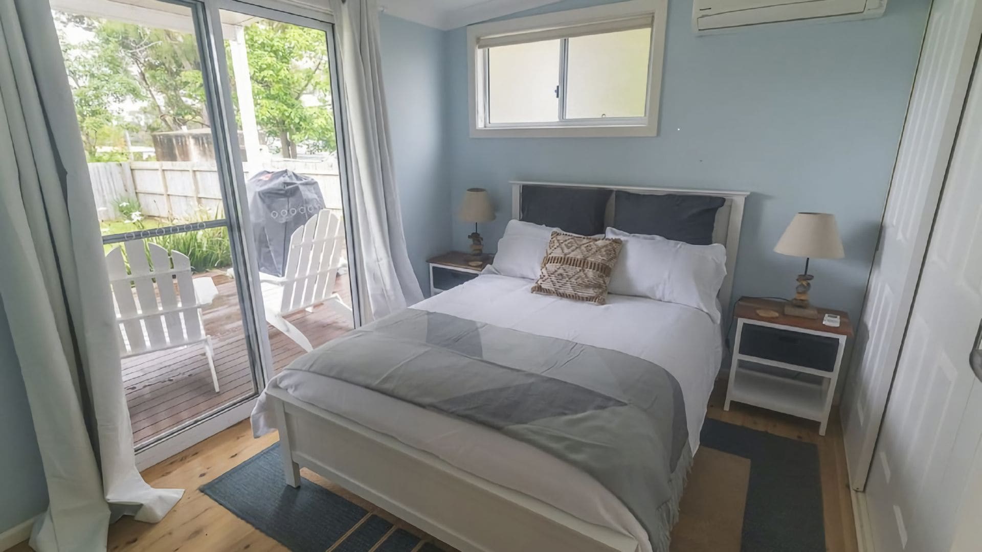 A bedroom with a bed, two bedside tables, a window, and a view of the outdoors.