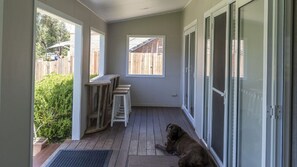 Eine überdachte Veranda mit Holzdeck, einem kleinen Tisch und einem Hund.