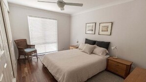 A bedroom with a bed, nightstands, a chair, a ceiling fan, and a window with blinds. - Saltwater ~ Cozy sanctuary by the sea (Bendalong)