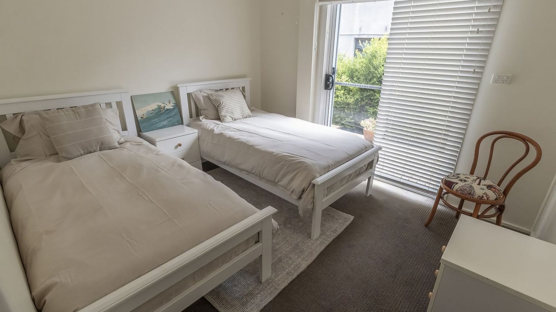 A bedroom with two beds, a nightstand, a chair, and a window with blinds.