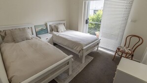 Una camera da letto con due letti, un comodino, una sedia e una finestra con persiane.