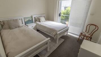 A bedroom with two beds, a nightstand, a chair, and a window with blinds.