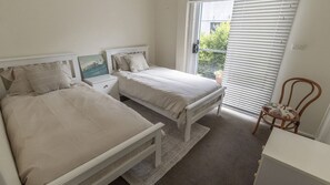 A bedroom with two beds, a nightstand, a chair, and a window with blinds. - Saltwater is a pet friendly home in Bendalong (Bendalong)