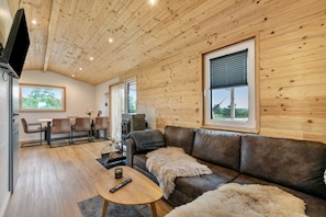 Ein gemütliches Blockhaus-Interieur mit Holzbalkendecke, Ledersofa, Essbereich und Kamin.