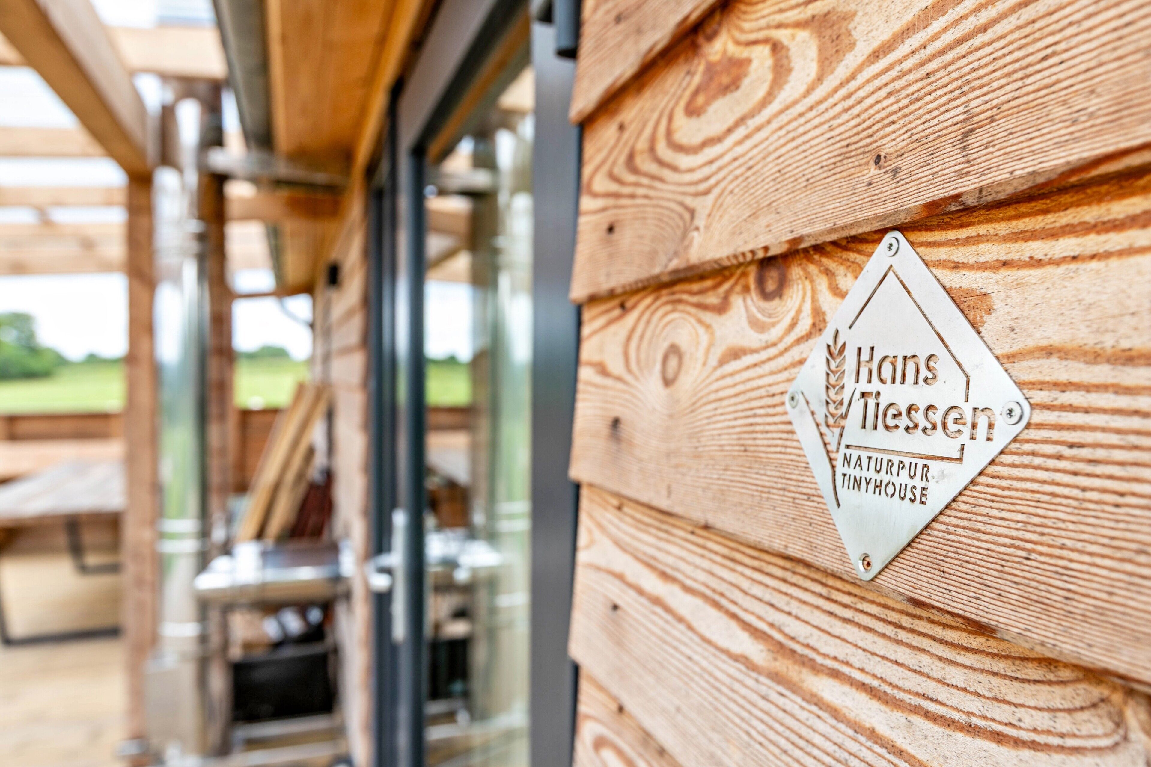 En træfacade med et skilt, der siger 'Hans/Tissen NATURPUR TINYHOUSE'.