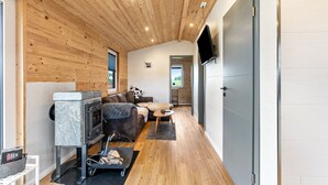 Een modern interieur met een houten plafond, een stenen openhaard, een bank, een televisie en uitzicht door een deur.