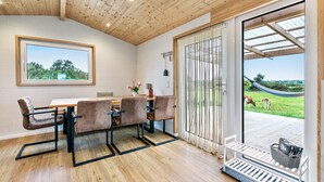 Een eetruimte met een houten tafel en stoelen, uitzicht op de omgeving en een deur naar een overdekt terras.