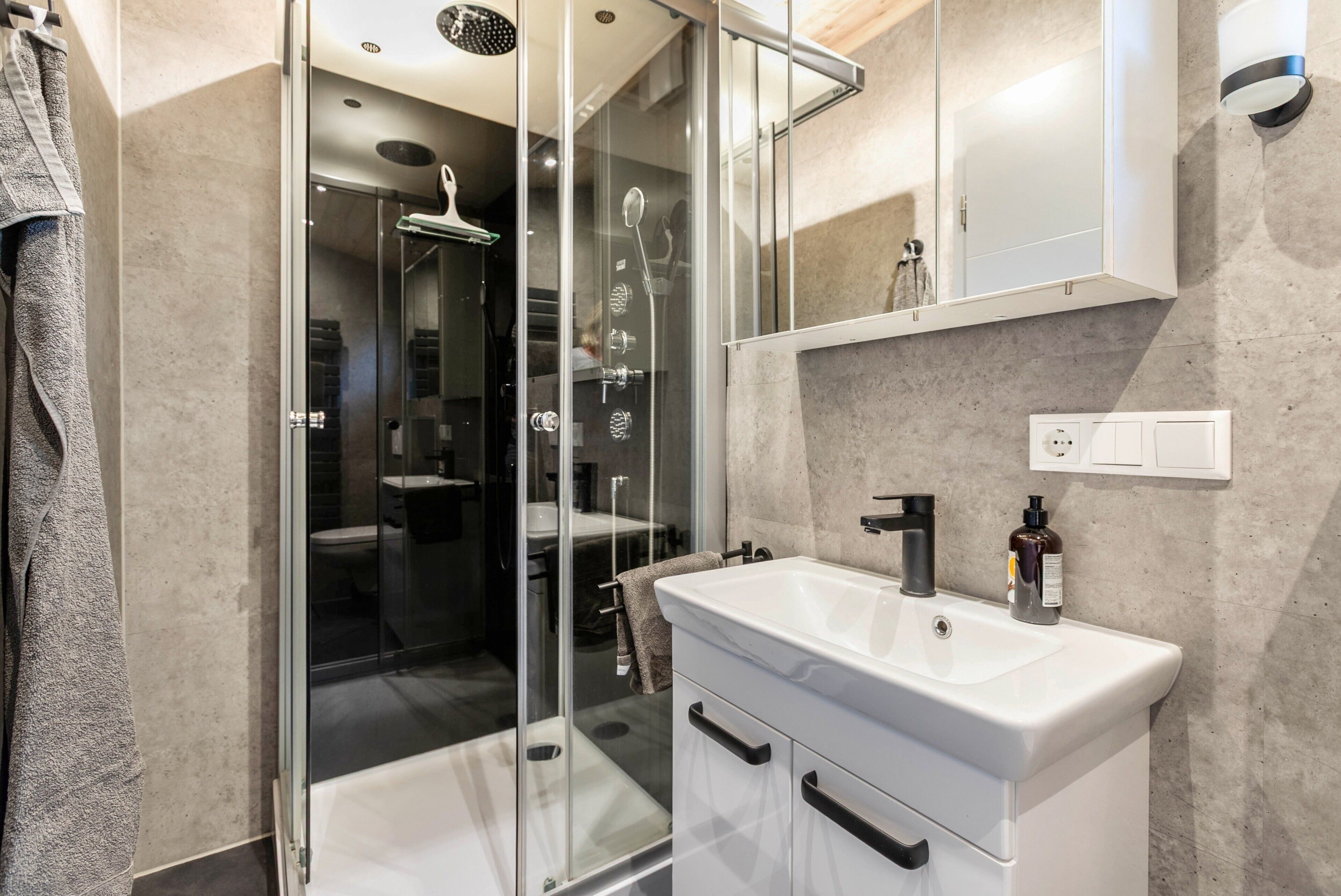Une salle de bain moderne avec une douche à parois de verre, un lavabo blanc et un miroir au-dessus du lavabo.