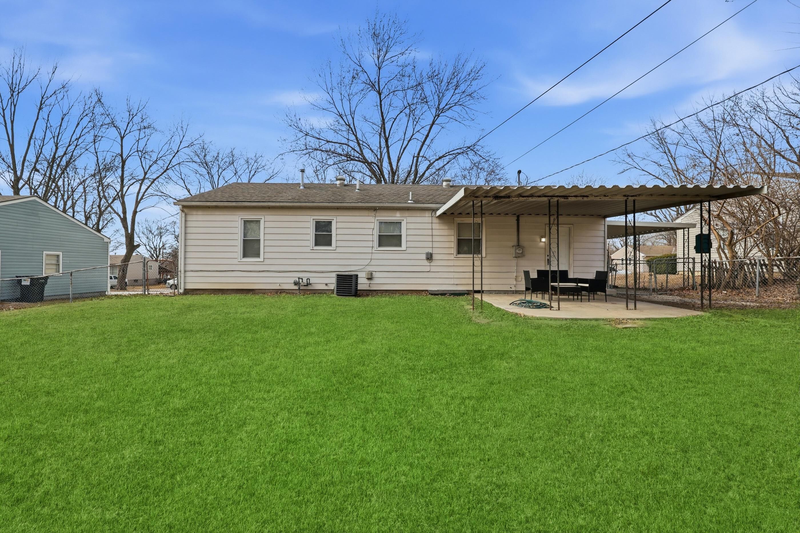 A single-story house with a covered patio area, a lawn, and a tree in the background.