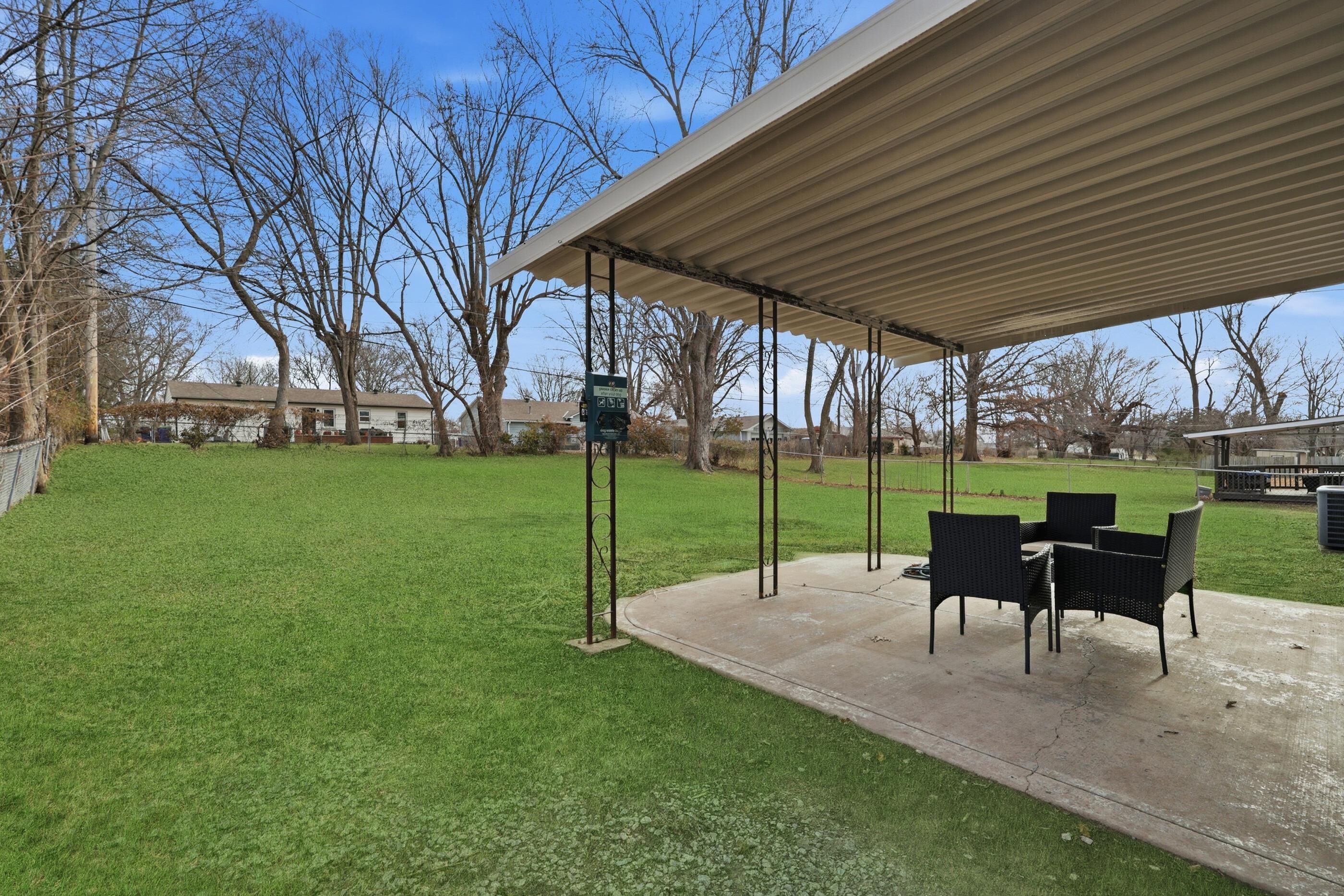 An outdoor patio with a covered seating area, a concrete floor, and a grassy lawn.