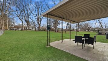 An outdoor patio with a covered seating area, a concrete floor, and a grassy lawn.