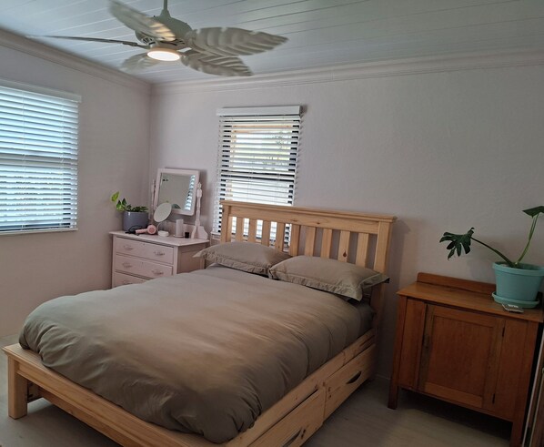 Ein Schlafzimmer mit einem hölzernen Bett, einem Deckenventilator, einem Schminktisch und einer Topfpflanze.