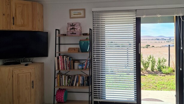 Un dormitorio con cama, armarios de madera, estantería, televisor y ventana corredera que da a un campo.
