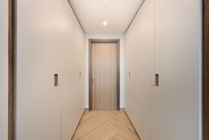 A hallway with a wooden door at the end, flanked by white walls and a wooden floor. - 2501-Bloomfields Luxurious 3BR  West Res (Dubai)