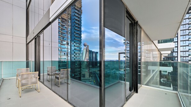 A modern balcony with glass walls, offering a view of tall buildings and a cityscape. - 2501-Bloomfields Luxurious 3BR  West Res (Dubai)