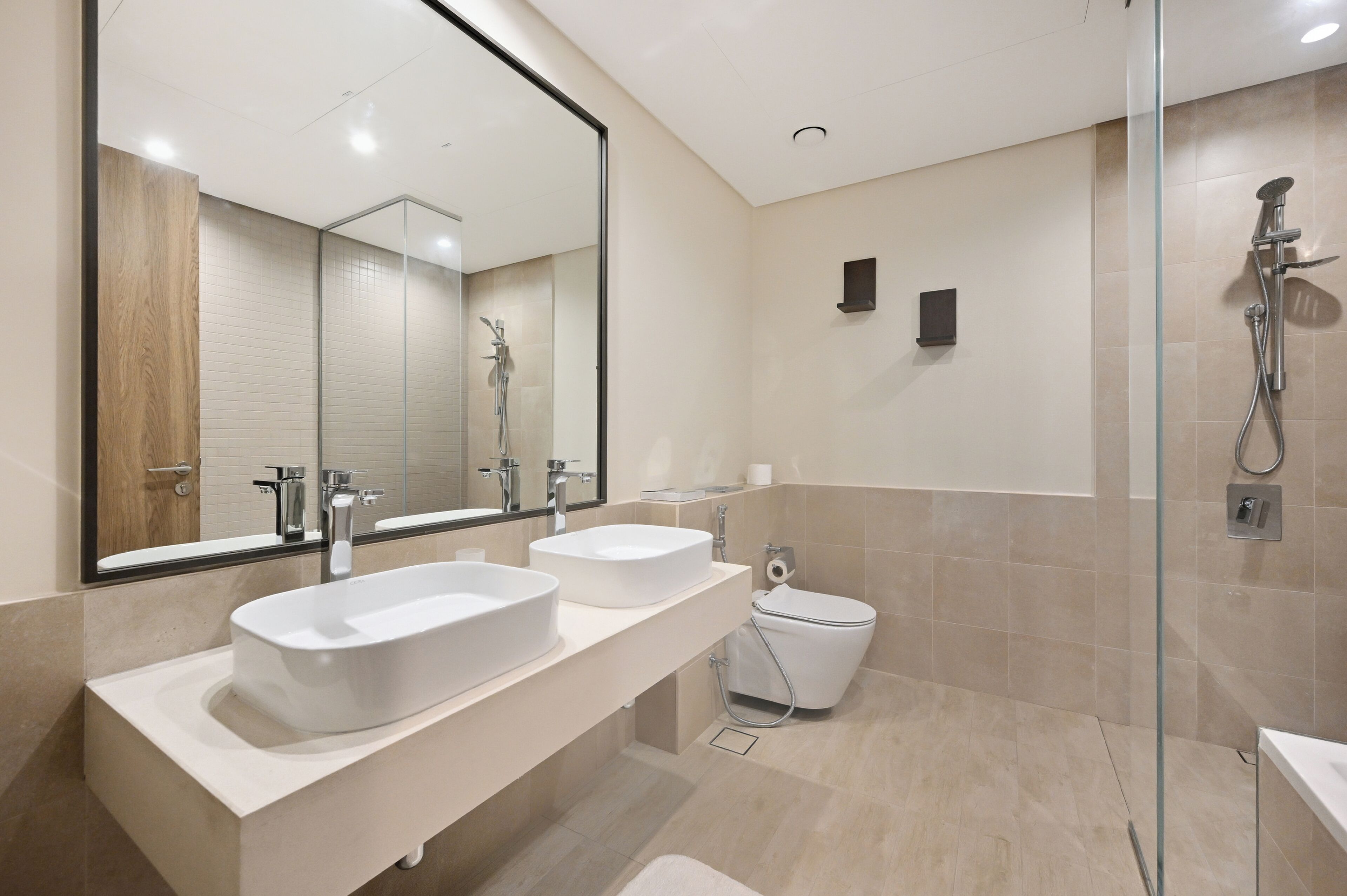 A modern bathroom with two sinks, a glass shower enclosure, and a toilet.