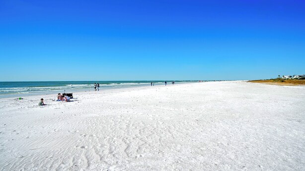 A wide sandy beach with footprints and a few people walking.