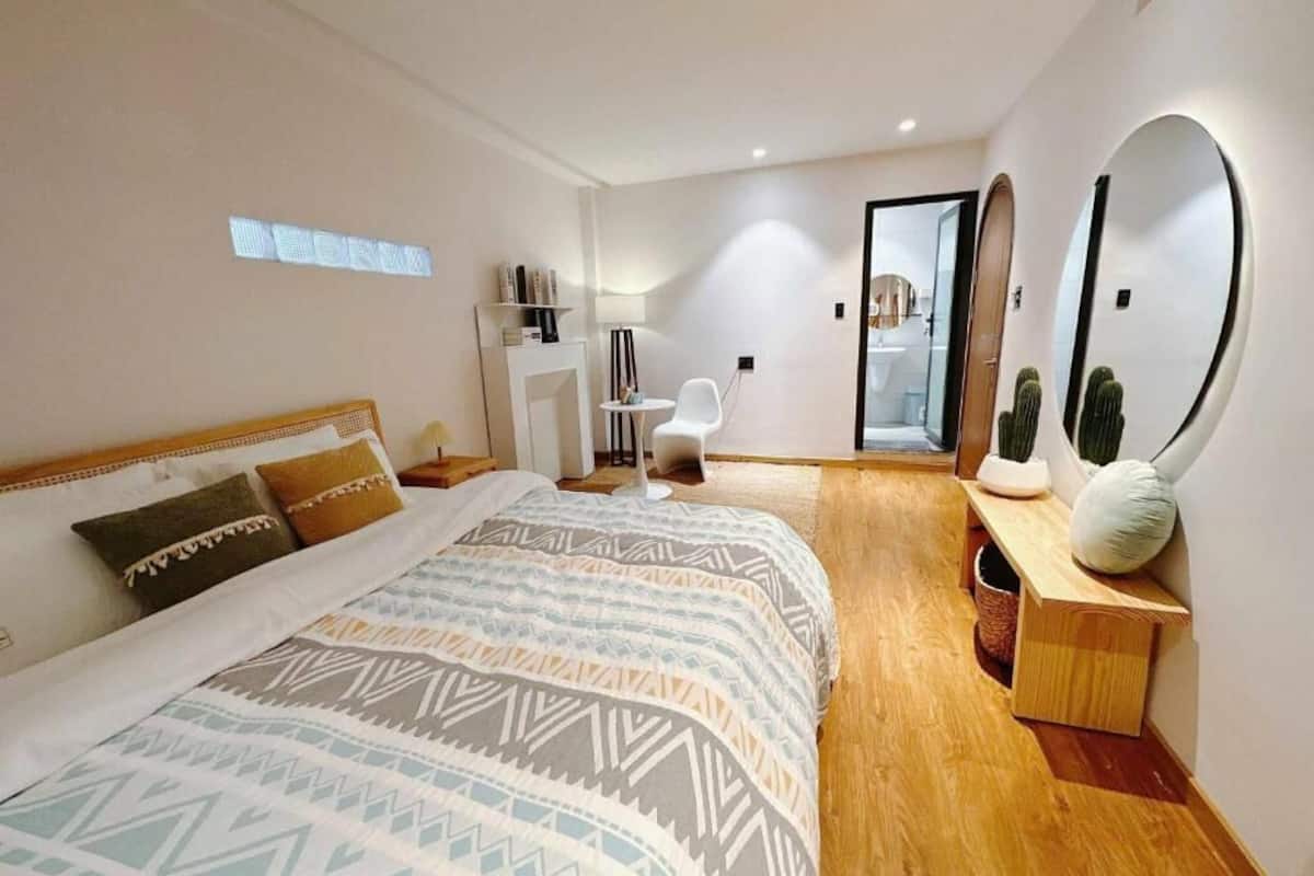 A modern bedroom with a large bed, bedside tables, a mirror, and a small seating area.