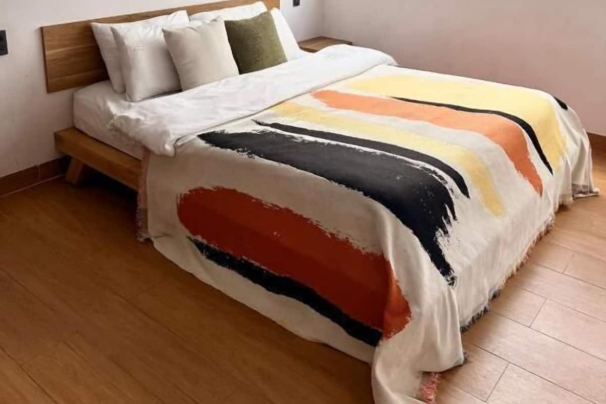 A bedroom with a bed, a window with a city view, and a painting on the wall.