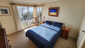 Un dormitorio con una cama grande, una silla, una mesita de noche, una lámpara y una ventana con cortinas.