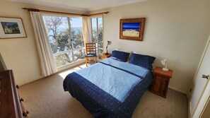 A bedroom with a large bed, a chair, a nightstand, a lamp, and a window with curtains. - Southern Comfort has ocean views (Manyana)