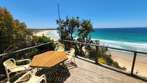Eine Holzterrasse mit Tisch und Stühlen mit Blick auf einen Strand.