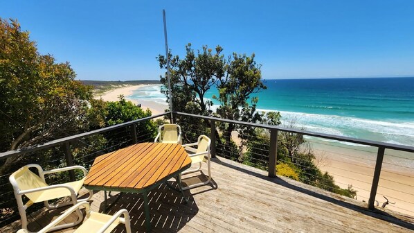 Eine Holzterrasse mit Tisch und Stühlen mit Blick auf einen Strand.