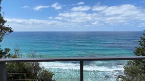 Blick auf das Meer von einem Balkon mit Geländer, Bäumen und blauem Himmel.
