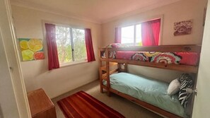 Une chambre avec un lit superposé, une fenêtre, une petite armoire en bois et une œuvre d’art colorée accrochée au mur.