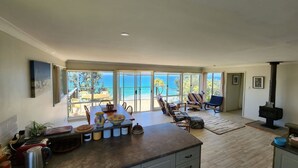 Un'ampia zona giorno con una grande finestra vista spiaggia, una cucina con isola centrale e un camino.