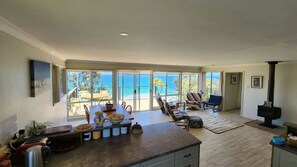 Ein geräumiger Wohnbereich mit großem Fenster mit Blick auf einen Strand, eine Küche mit Kochinsel und ein Kamin.